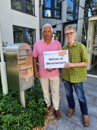 Andreas Fateh und Herbert Looschelders halten ein Plakat in die Kamera "Wohnen ist Menschenrecht"