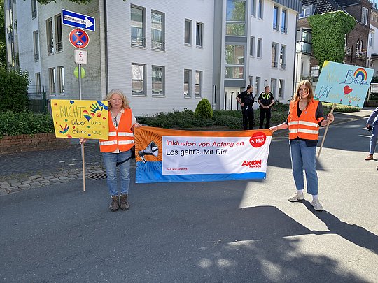 Monika van Bebber und Franziska Rütjes halten ein Plakat von Aktion Mensch