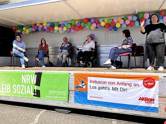Auf der Bühne die Moderatorin und die teilnehmenden Personen der Podiumsdiskussion