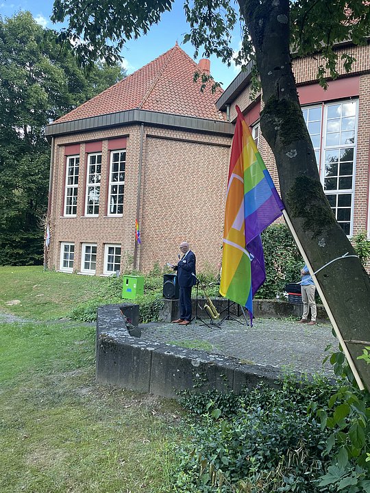 Der Landrat im Hintergrund. Im Vordergrund die paritätische Regenbogenfahne