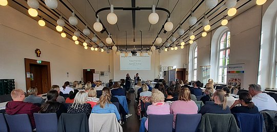 Menschen sitzen in Reihen und hören dem Vortrag zu